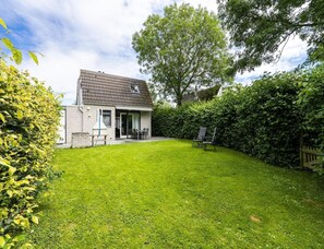 A house with a tiled roof, a lawn, and a patio area with chairs. - Home Near Vlissingen Beach (Vlissingen)