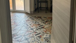 A room with a tiled floor, a wooden door, and a small table with a chair. - La Corte di Pirandello (Agrigento)