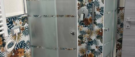 A glass-enclosed shower with a tropical leaf pattern on the walls.