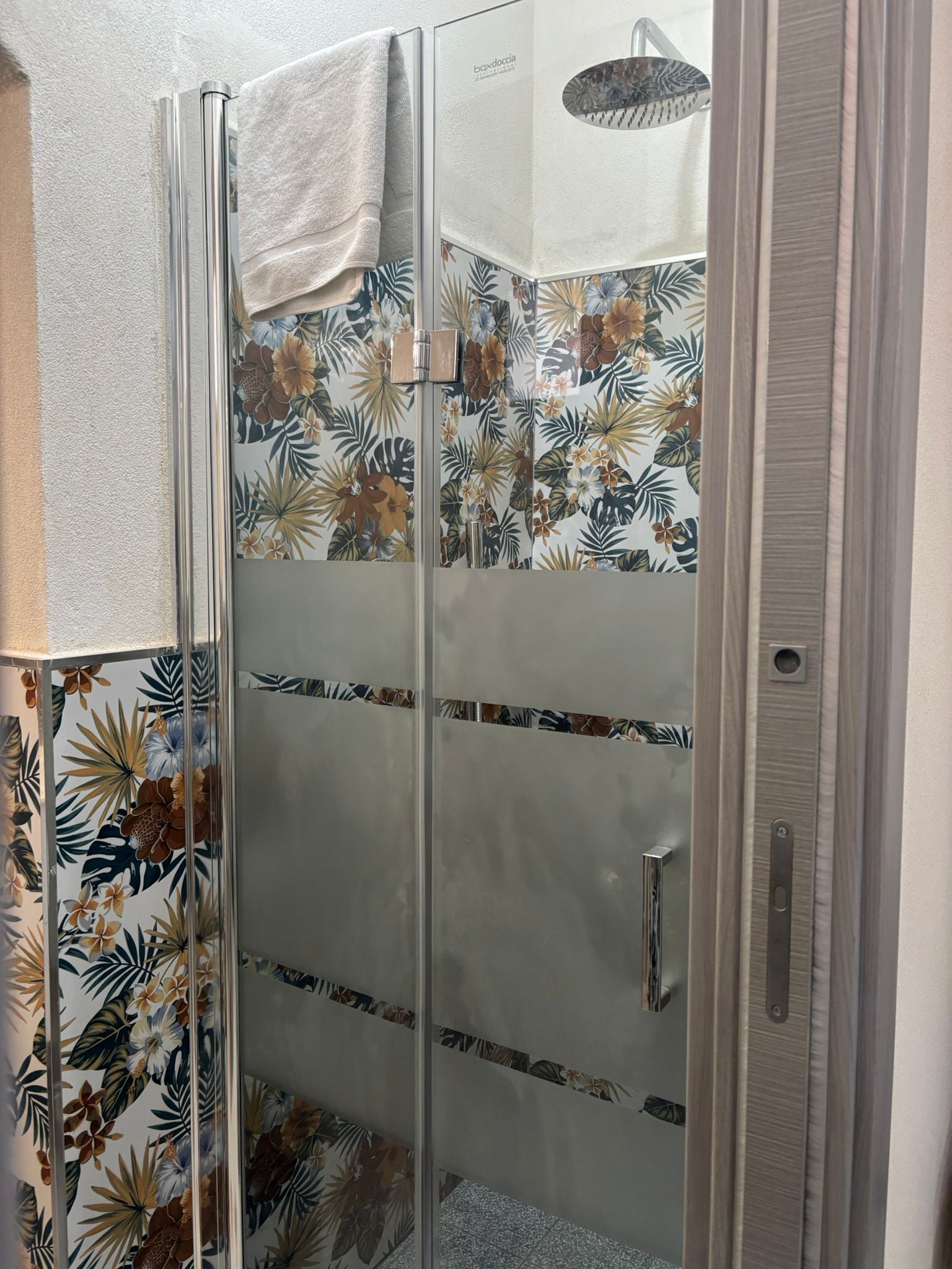 Una cabina doccia in vetro con motivo a foglia tropicale sulle pareti.