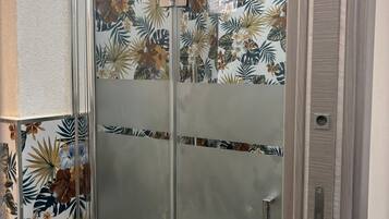 Una cabina doccia in vetro con motivo a foglia tropicale sulle pareti.