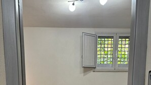 A room with two beds, a window with a view of greenery, and a patterned floor. - La Corte di Pirandello (Agrigento)