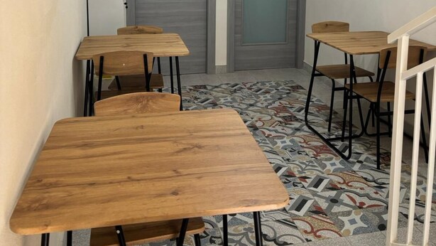 A room with multiple wooden tables and chairs, a patterned floor, and two doors in the background. - La Corte di Pirandello (Agrigento)