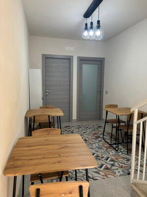 Una habitación con varias mesas y sillas de madera, piso con diseño y dos puertas al fondo.