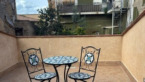 A patio with a round table and two chairs, surrounded by a low wall and a view of buildings. - La Corte di Pirandello (Agrigento)