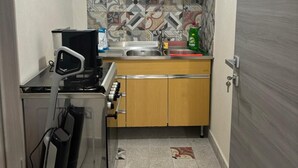 A compact kitchen with wooden cabinets, a tiled backsplash, a sink, and a coffee machine. - La Corte di Pirandello (Agrigento)