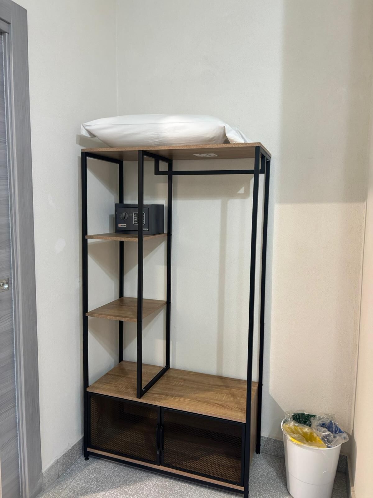 Una cama litera con colchón arriba, un pequeño estante con una radio y un cesto de basura.