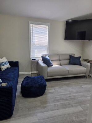 A living room with a sofa, ottoman, and a television mounted on the wall.