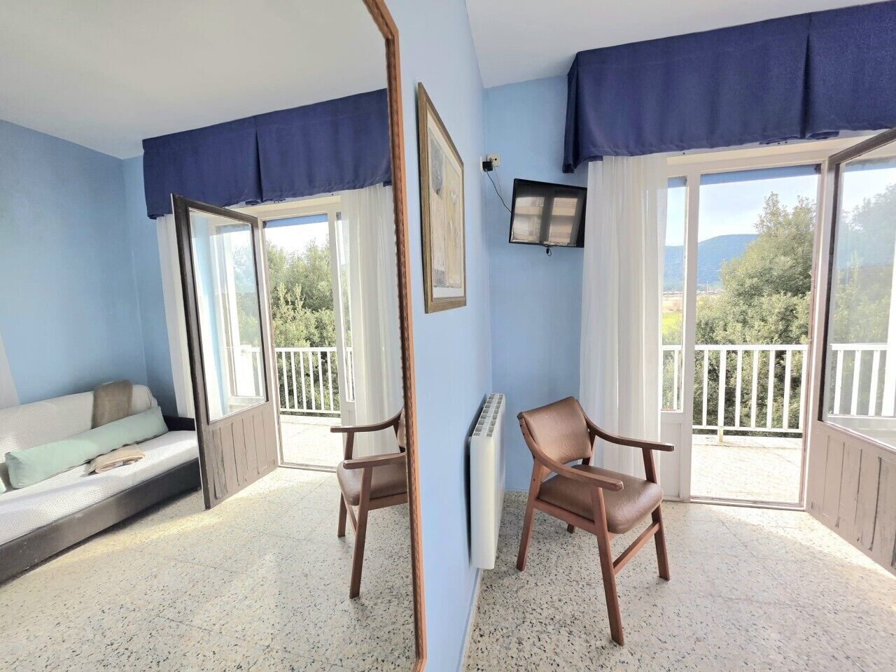Una habitación con cama, sillón, televisor y balcón con vistas.