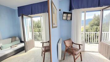 Una habitación con cama, sillón, televisor y balcón con vistas.