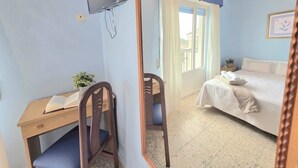 A room with a bed, a desk, a chair, a television, and a window with curtains.