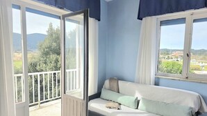 A room with a sofa, a window with curtains, and a balcony with a railing.