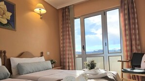 A hotel room with two beds, a window with curtains, a chair, and a small table.