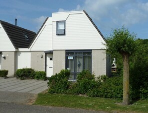 A two-story building with a sloped roof, a small window on the upper floor, and a door with a sign. - Home With Dune Views (Vlissingen)