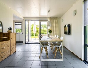 A modern kitchen with a wooden cabinet, a dining table with chairs, and a large window. - Home With Dune Views (Vlissingen)