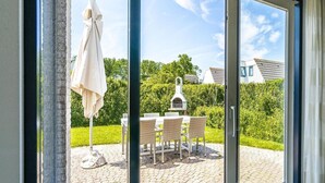 Porta de vidro dá acesso a um pátio externo com mesa, cadeiras, churrasqueira e um guarda-sol branco.