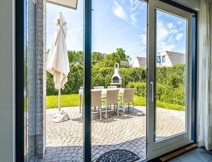 A glass door leading to an outdoor patio with a table and chairs, a grill, and a white umbrella. - Home With Dune Views (Vlissingen)