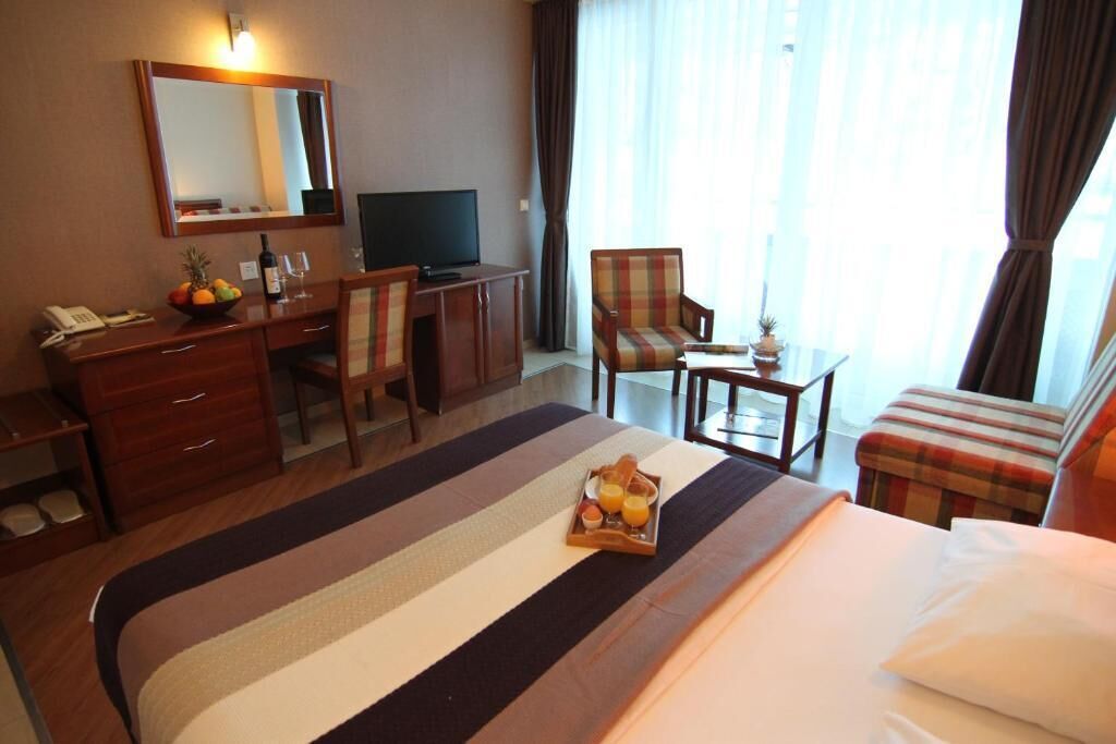 Habitación de hotel con cama, escritorio, televisor, silla y una mesita con bandeja de desayuno.