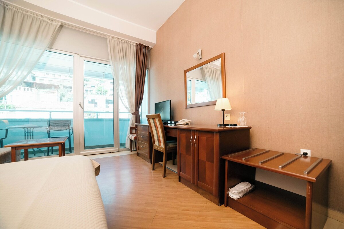 A hotel room with a bed, a desk, a chair, a television, a lamp, and a window with curtains.