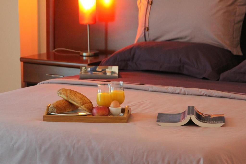 A neatly made bed with a tray of breakfast items, including bread, fruit, and orange juice, and an open book beside it.