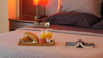 A neatly made bed with a tray of breakfast items, including bread, fruit, and orange juice, and an open book beside it.