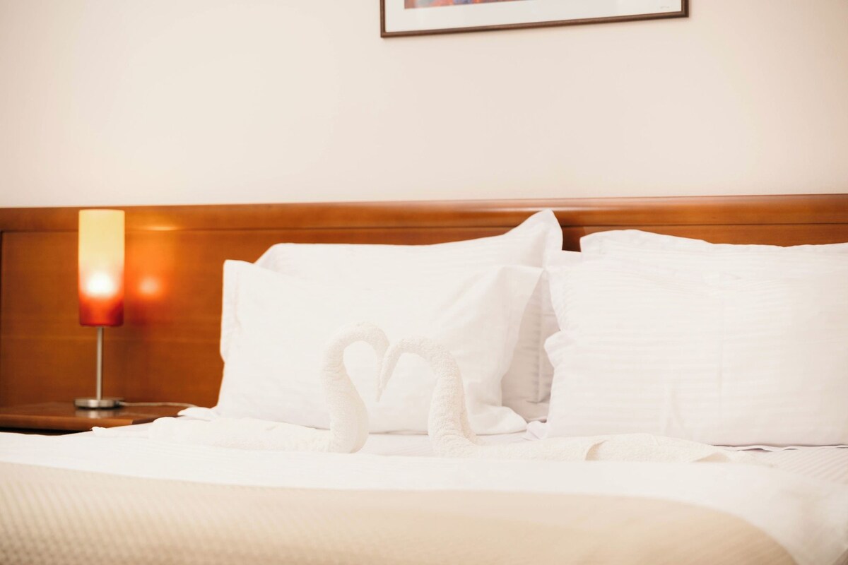 A neatly made bed with white linens and pillows, a bedside lamp, and a framed picture on the wall.
