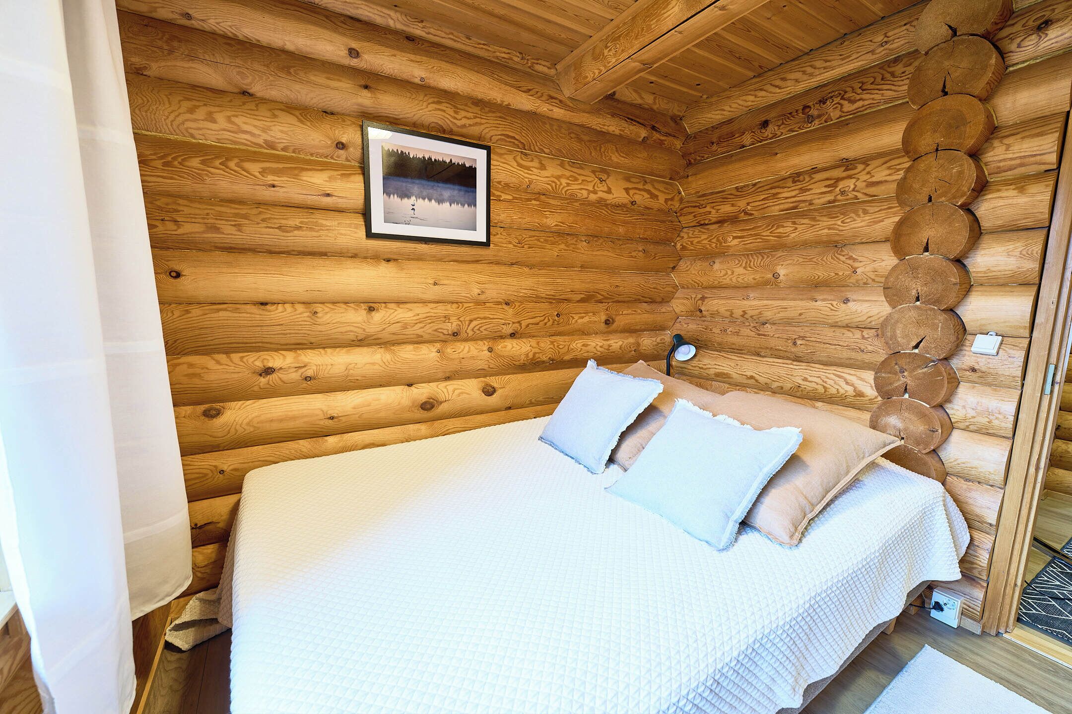 Una habitación tipo cabaña de madera con cama, almohadas, un cuadro enmarcado y una lámpara fijada a la pared.
