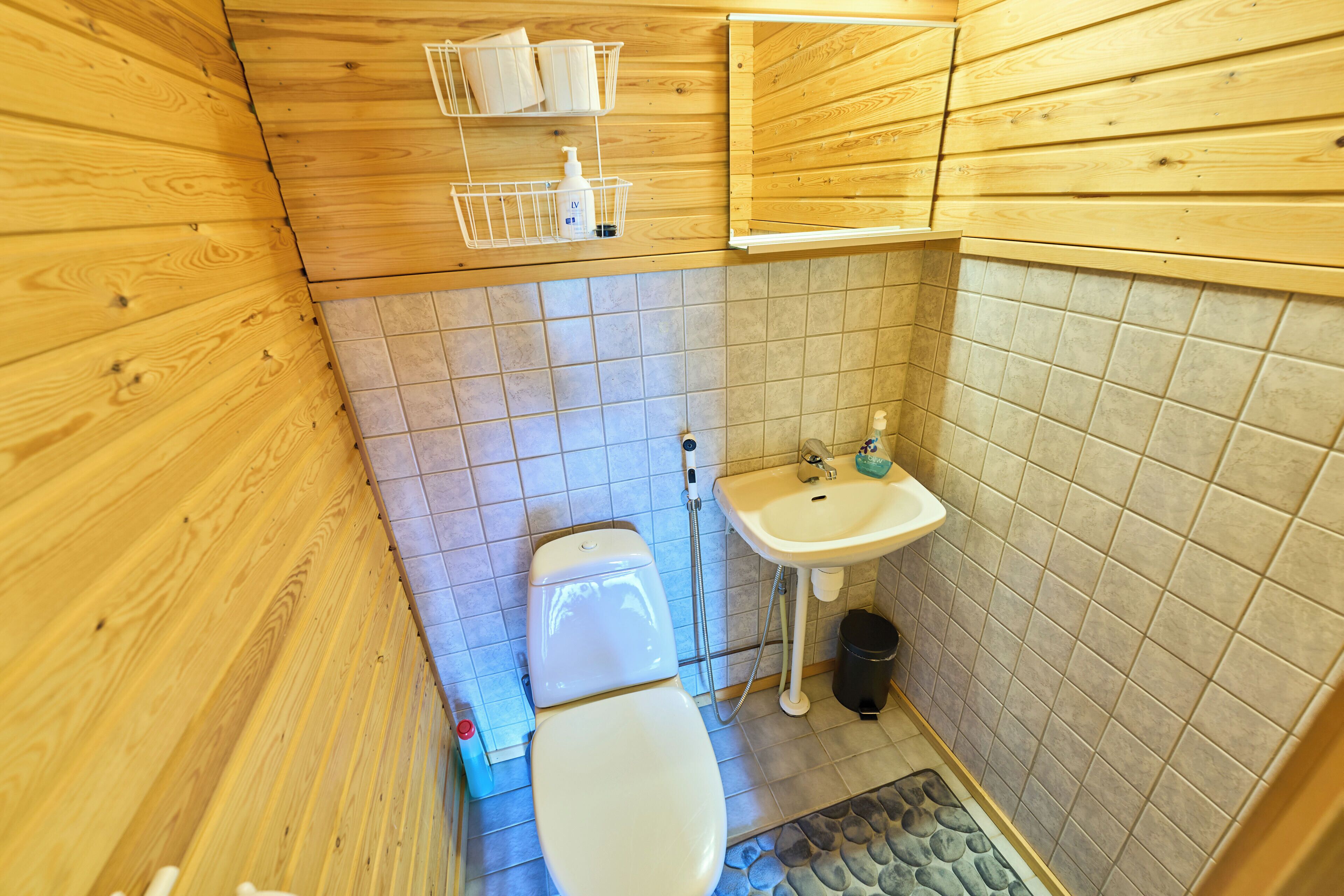 Un baño con paneles de madera, inodoro, lavabo y suelo de baldosas.