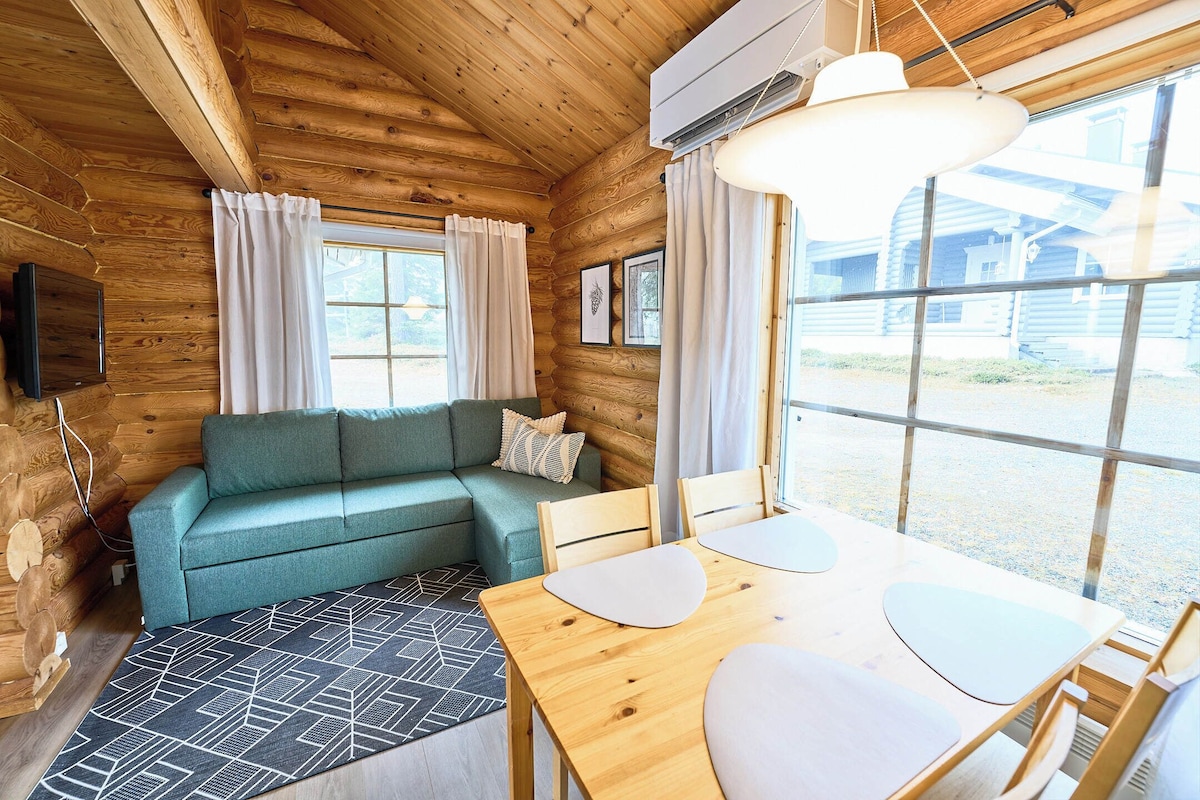 A wooden cabin interior with a sofa, dining table, and large windows.