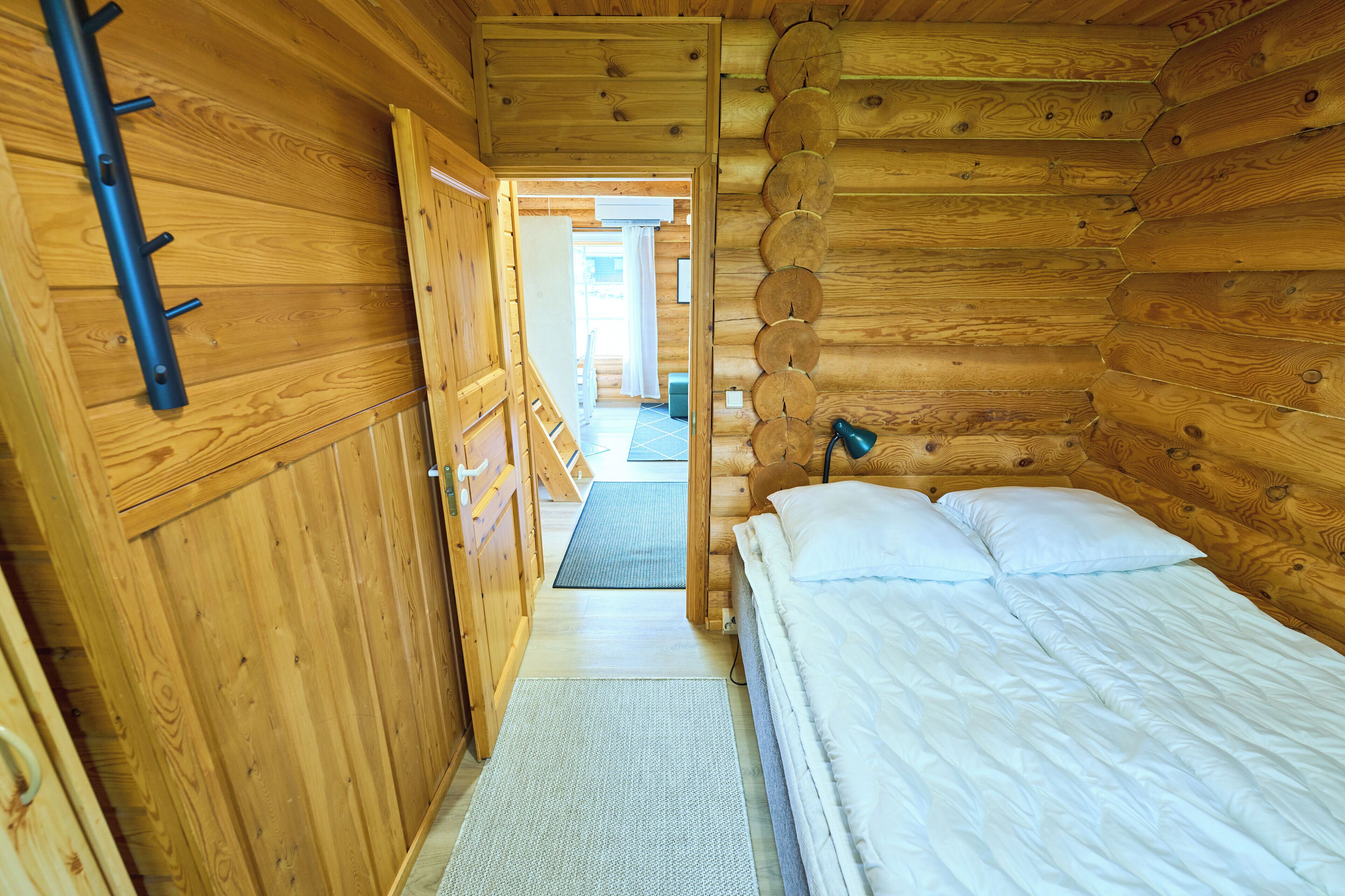 Interior de una cabaña de madera con una cama, una puerta que da a un pasillo y una pared de madera con diseños circulares.