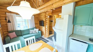 L’intérieur d’une cabane en rondins comprend une table à manger en bois, un canapé vert, un coin cuisine avec un lave-vaisselle blanc et un escalier en bois.