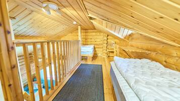A wooden cabin with a loft bedroom, a small seating area, and a visible staircase.