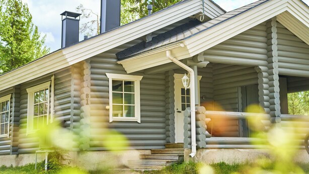 Une cabane en rondins avec un porche, une cheminée et une fenêtre.