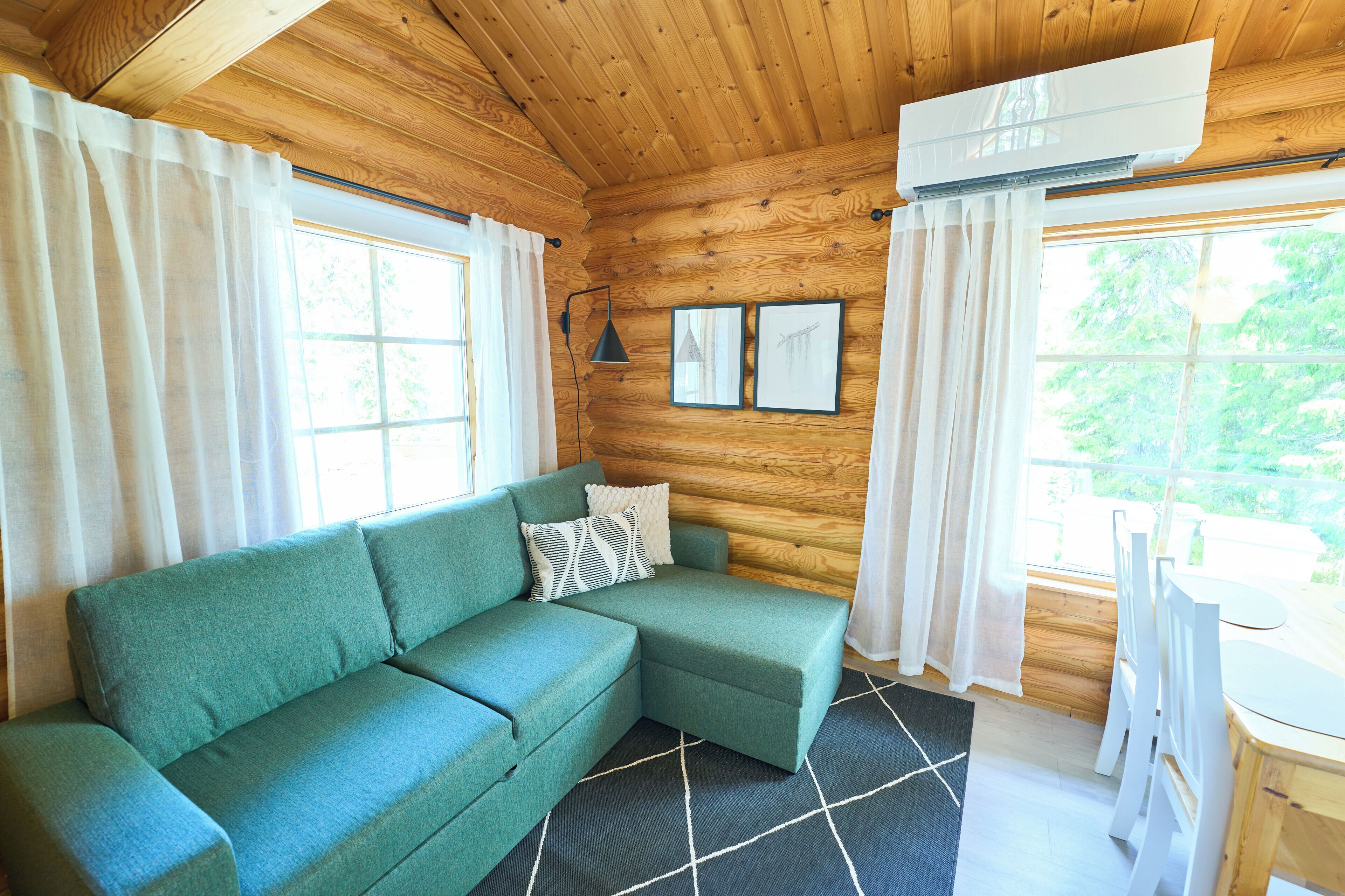 L’intérieur d’un chalet en bois, avec un canapé vert, une table à manger et une fenêtre avec des rideaux.