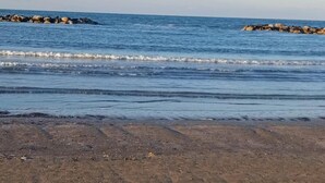 Uma praia com ondas calmas, um molhe rochoso e céu claro.