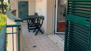 Uma varanda com mesa e cadeiras, uma porta verde e um relógio na parede.