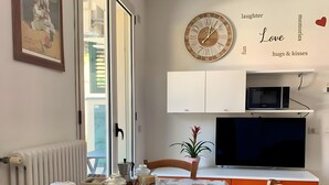 Uma sala de jantar com uma mesa posta para dois, um relógio, um micro-ondas e uma TV em um armário branco.