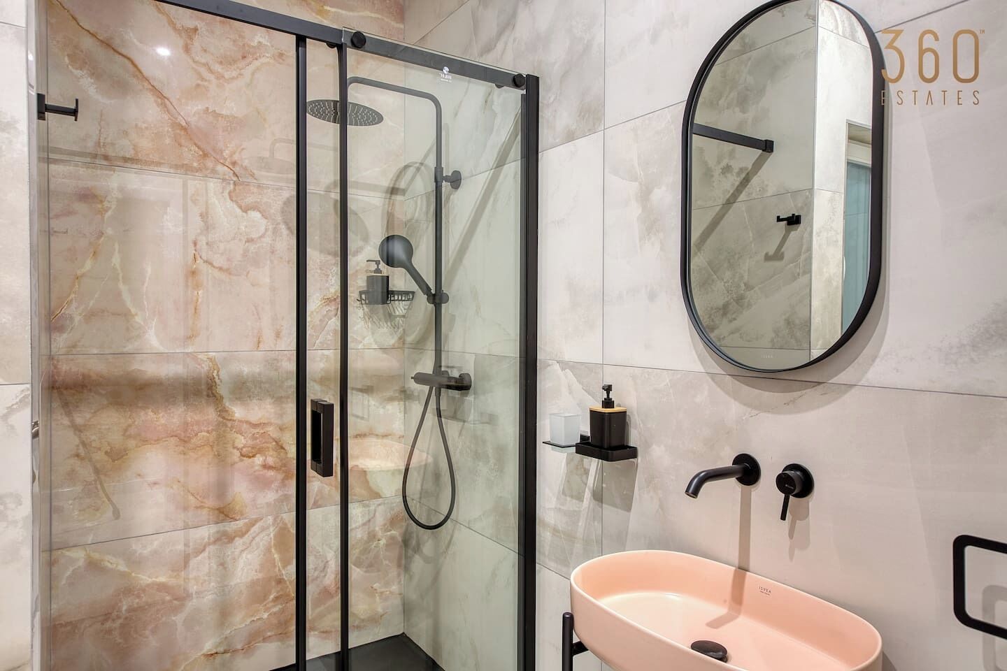 A modern bathroom with a glass-enclosed shower, a round mirror, and a pink sink.