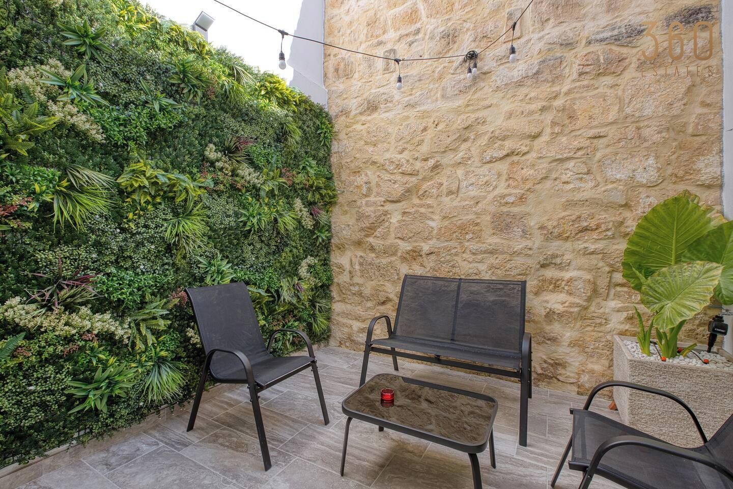 A patio with a stone wall, a green vertical garden, and two metal chairs and a table.