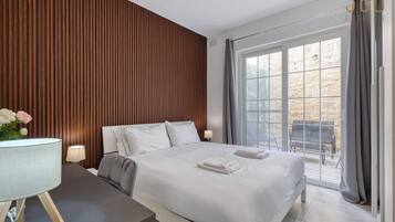 A modern hotel room with a large bed, a desk with a lamp, and a view of the outdoor patio.