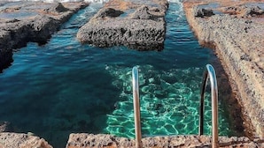Eine felsige Küstenlinie mit klarem Wasser und Metallstufen, die ins Meer führen.