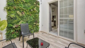 Eine Terrasse mit vertikalem Grünstreifen, einer Schiebetür und einem kleinen Tisch mit Kerze.