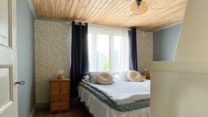 A bedroom with a wooden ceiling, a bed with white bedding, a dresser, and a window with curtains. - 4 Person Holiday Home in Farjestaden (Farjestaden)