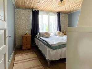 A bedroom with a wooden ceiling, a bed with white bedding, a dresser, and a window with curtains. - 4 Person Holiday Home in Farjestaden (Farjestaden)