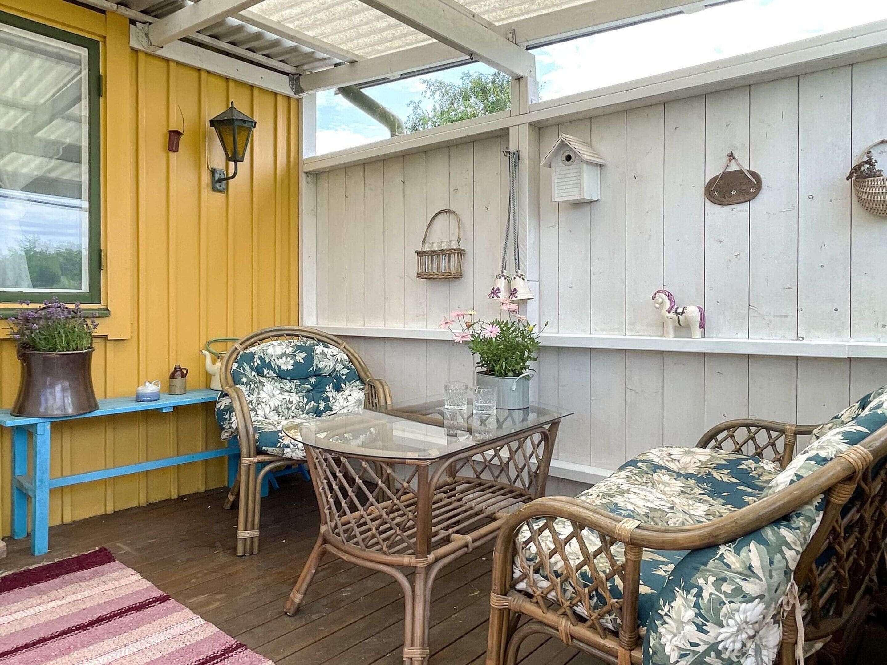 A covered patio with wicker furniture, a glass table, and decorative items on the walls.