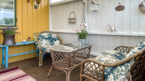 A covered patio with wicker furniture, a glass table, and decorative items on the walls. - 4 Person Holiday Home in Farjestaden (Farjestaden)