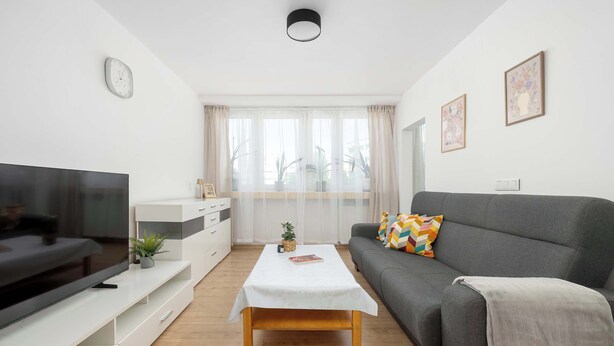 A living room with a TV, sofa, coffee table, and a window with curtains. - Cozy Apartment for 3 People | Great Location (Gliwice)