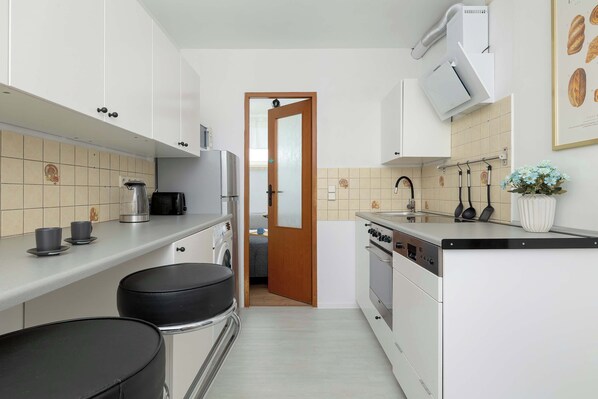 A modern kitchen with white cabinets, a stainless steel kettle, a coffee maker, and a dishwasher.