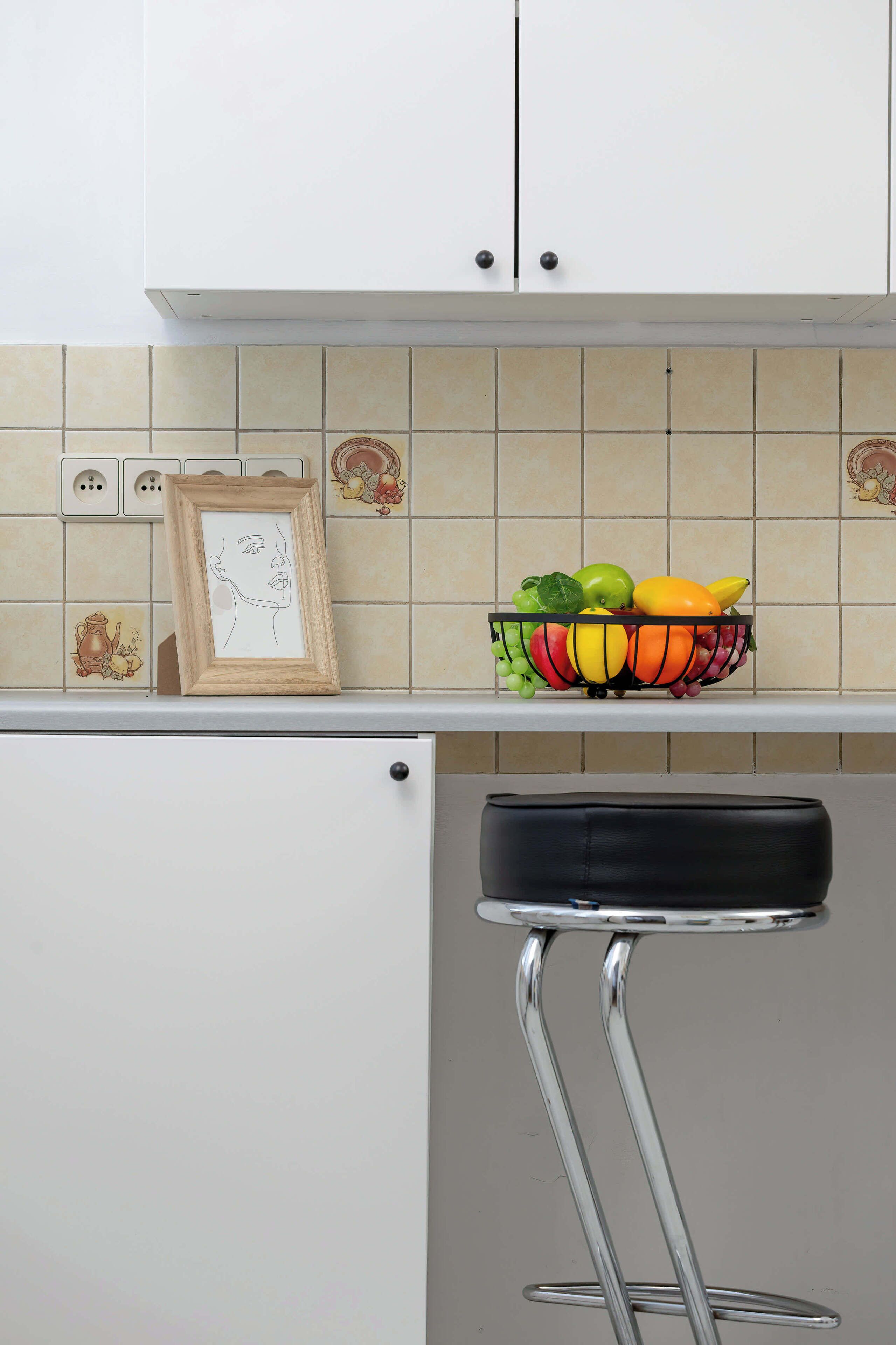 Una cocina con fruteros, un cuadro enmarcado y un taburete de bar.