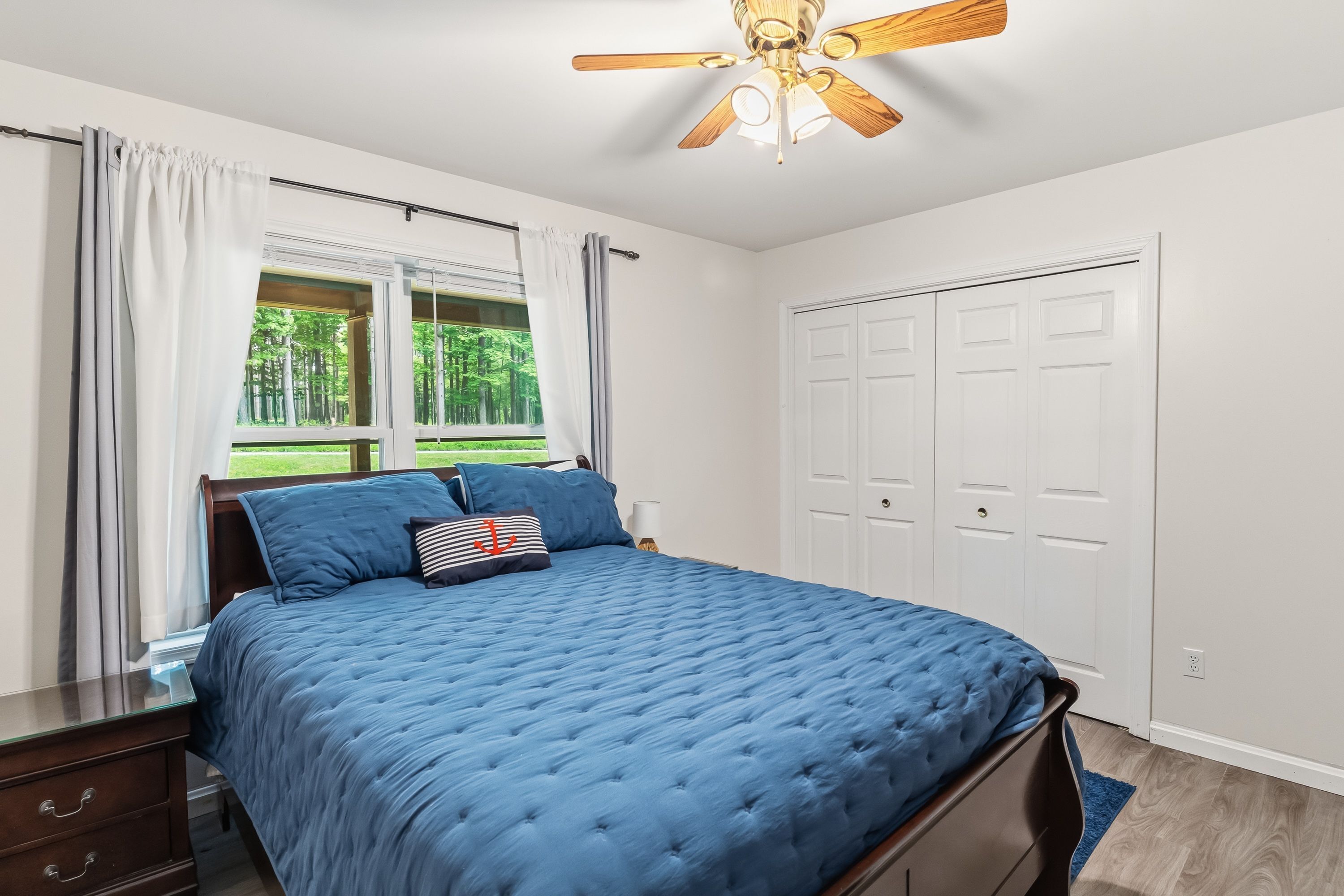 A bedroom with a bed, a ceiling fan, a window with curtains, and a white door.
